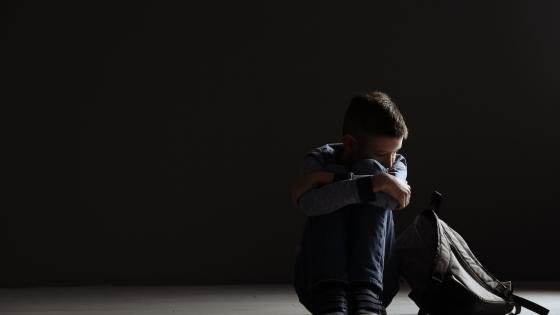 Upset child with backpack sitting in dark room