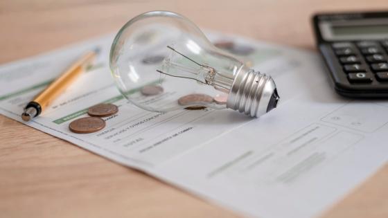 Electricity bill with light bulb, several coins, calculator and pen on the desk