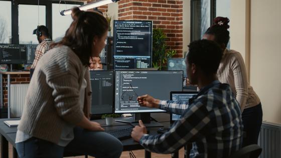 Programer sitting on desk discussing with mixed team of software developers about artificial intelligence innovation