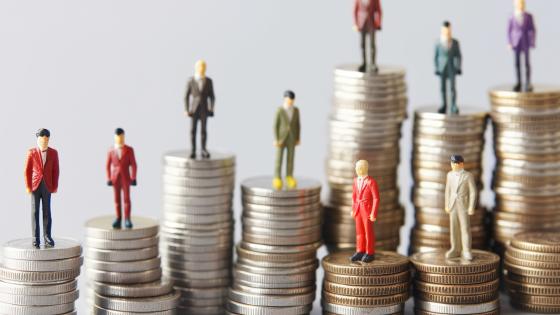 miniature figures standing on stacks of coins 