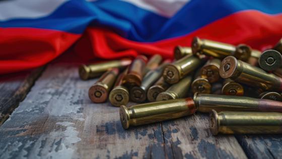 A Pile of Bullet Shells on a Wooden Table in front of Russian flag