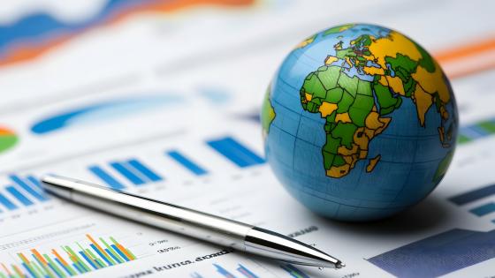 A globe sitting on a table with charts and a pen nearby